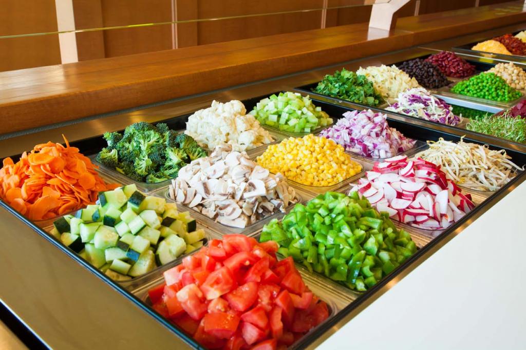 Overhead view of a salad bar with metal trays filled with chopped vegetables, legumes, and fresh produce