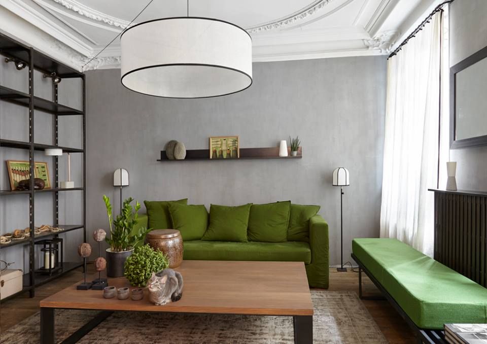 Modern living room with an olive green sofa, wooden coffee table, metal shelving, and gray walls with ornate ceiling molding